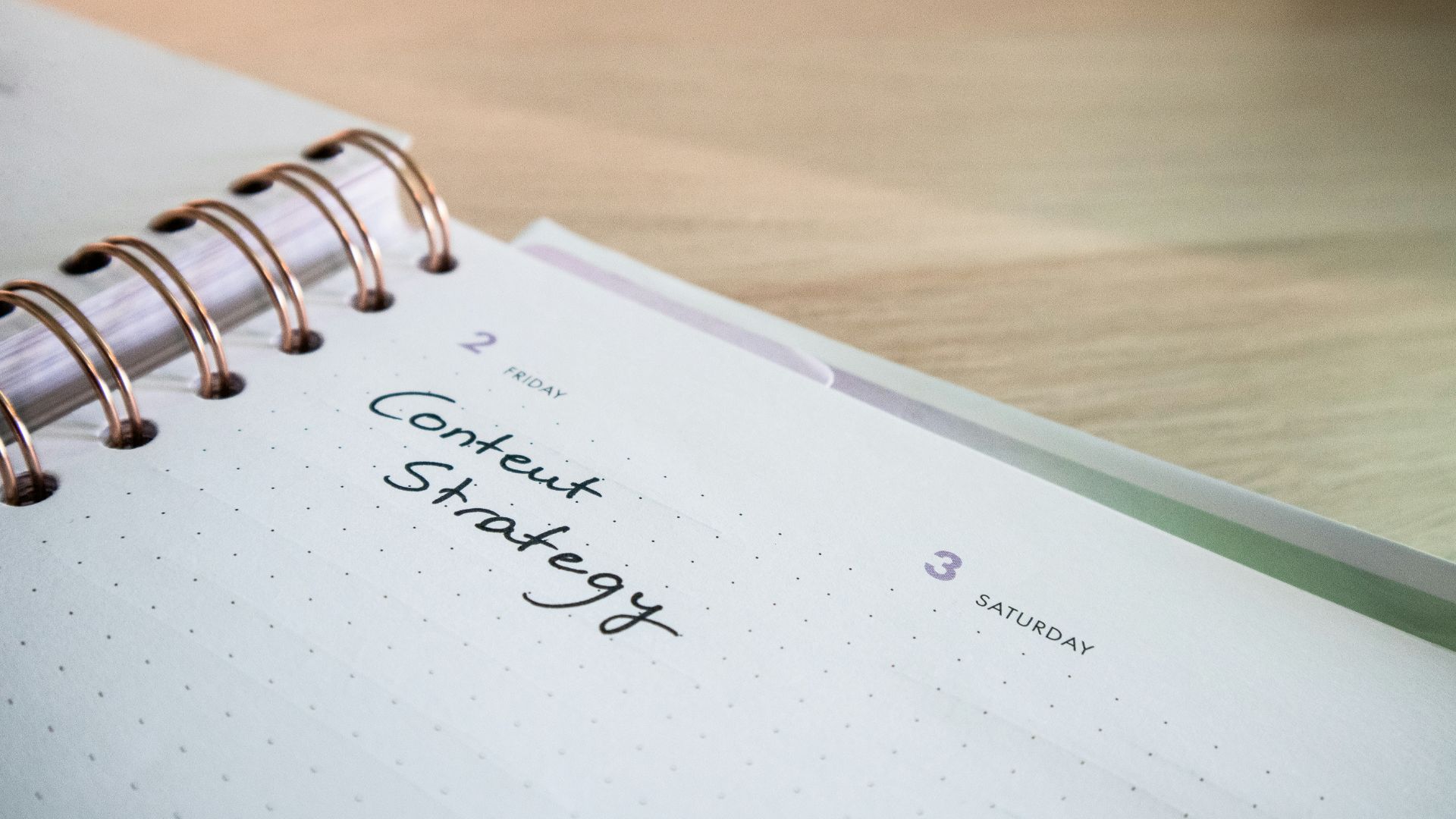 A planner open to a page showing "Friday 2" and "Saturday 3," with the handwritten note "Content Strategy" under Friday. It rests on a light wooden surface, ready to guide your next SEO marketing campaign.