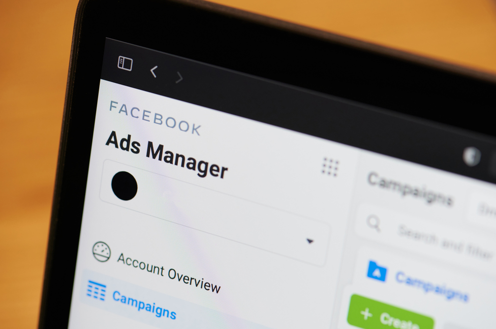 Close-up of a computer screen displaying the Facebook Ads Manager interface. The screen shows options like "Account Overview" and buttons for creating and managing campaigns. The background suggests the image is taken in a workspace.