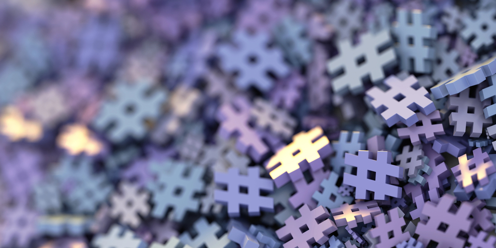 A close-up image featuring a large pile of three-dimensional hashtag symbols in various shades of blue and purple. The hashtag symbols are stacked and scattered, creating a textured and abstract appearance.